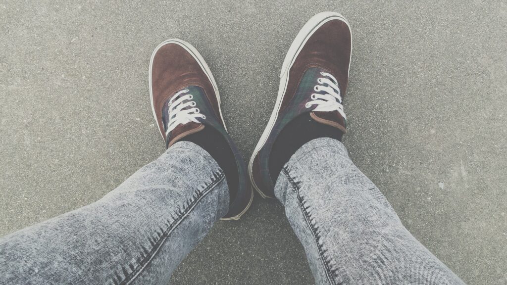 A pair of legs in jeans, wearing trainers.