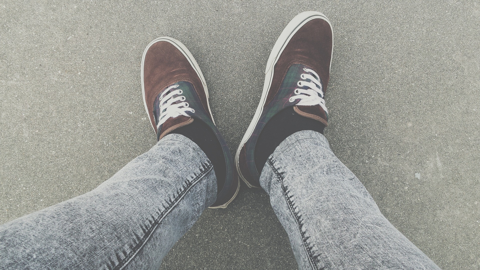 A pair of legs in jeans, wearing trainers.