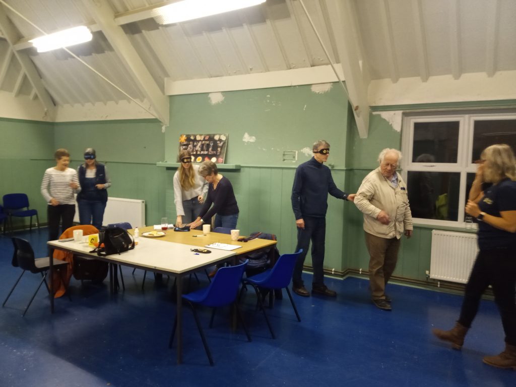People in pairs, one blindfolded, in a hall